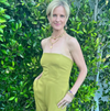 Woman in a green strapless jumpsuit standing in front of green foliage.