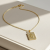 Gold necklace with a rectangular pendant on a beige surface