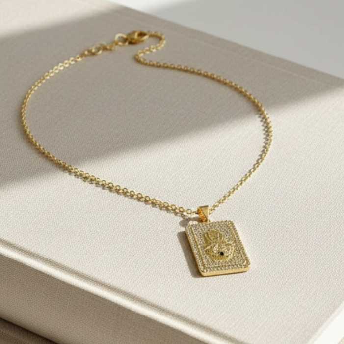 Gold necklace with a rectangular pendant on a beige surface