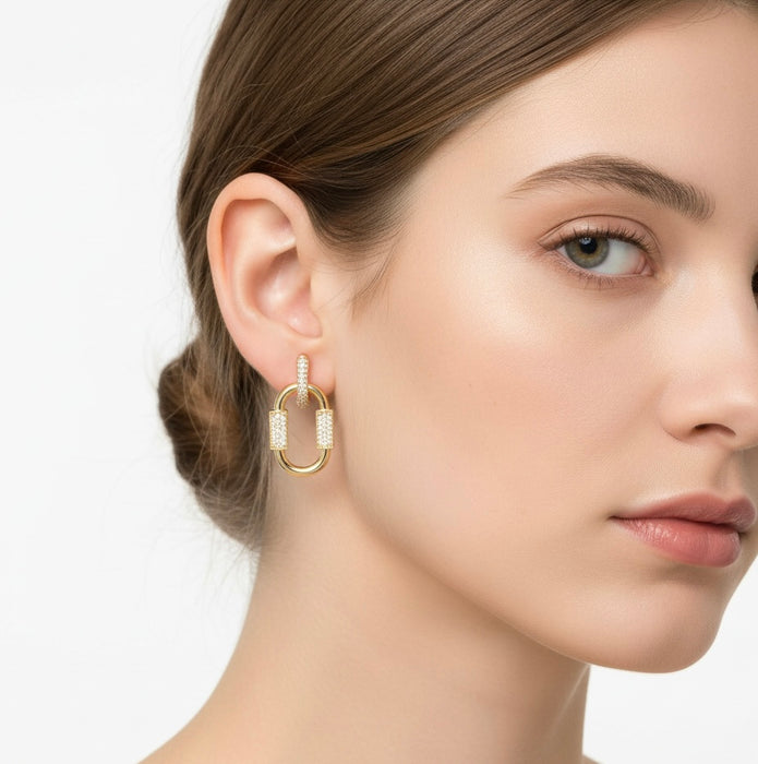 Close-up of a woman wearing gold hoop earrings with embedded stones on a neutral background