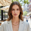 Woman wearing a light gray blazer and gold necklace on a city street.