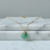 Gold necklace with a green pendant on a marble surface