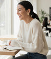 Woman in a white sweater sitting at a table in a bright room, smiling.