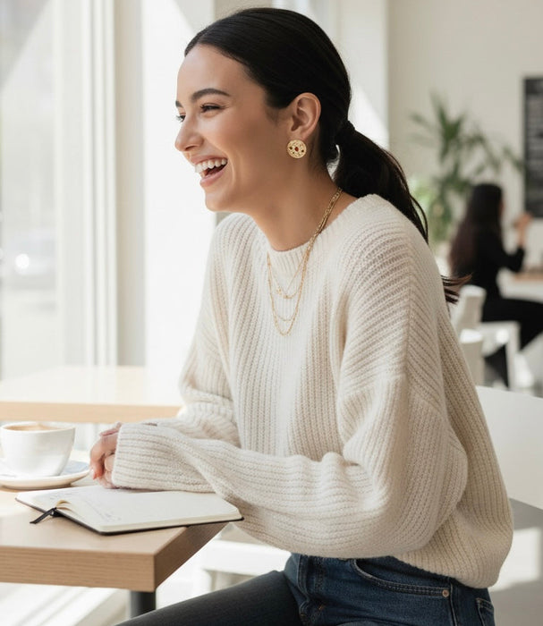 Woman in a white sweater sitting at a table in a bright room, smiling.