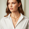 Woman wearing a gold necklace with a pendant against a neutral background