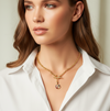Woman wearing a gold necklace with a pendant against a neutral background