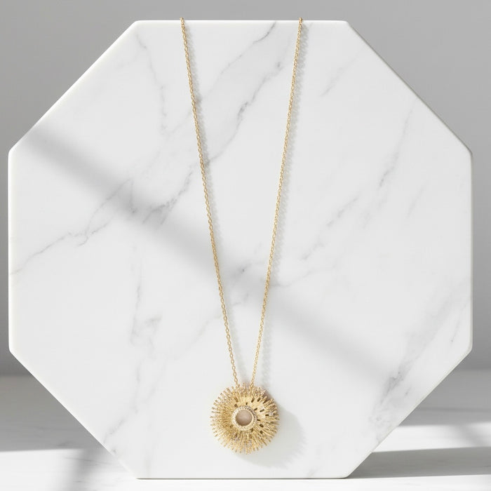 Gold necklace with a sunflower pendant on a marble surface