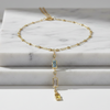 A delicate gold chain necklace with a central rectangular light blue gemstone and a dangling yellow gemstone, displayed on stacked white marble blocks.