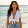 Woman in a white top and denim shorts standing on a beach.