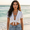 Woman in a white top and denim shorts standing on a beach.