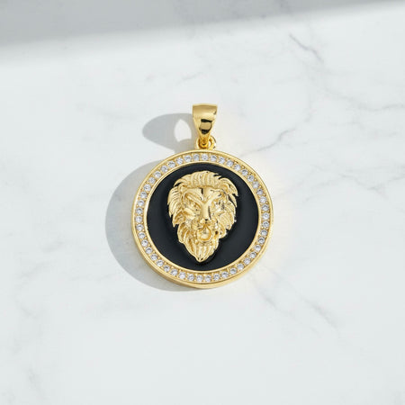 Gold lion head pendant with black center and clear stones on a white marble background