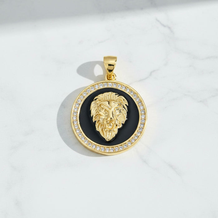 Gold lion head pendant with black center and clear stones on a white marble background