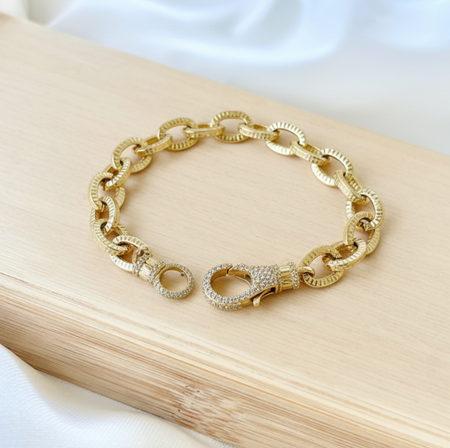 Gold chain bracelet on a wooden surface with a white fabric background