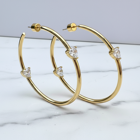 Gold hoop earrings with triangular gemstones on a marble surface