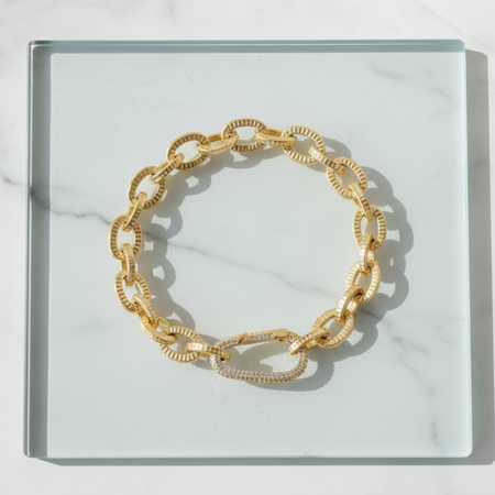 Gold chain bracelet on a clear glass surface with a marble background