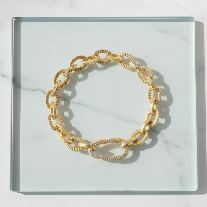 Gold chain bracelet on a clear glass surface with a marble background