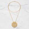 Gold necklace with a textured pendant on a marble surface