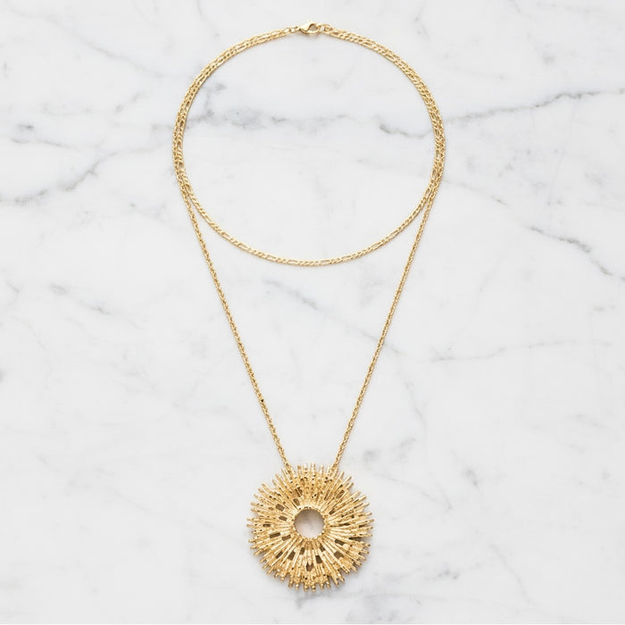 Gold necklace with a textured pendant on a marble surface