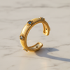A textured gold ring with three blue and white floral accents, displayed on a light marble surface.
