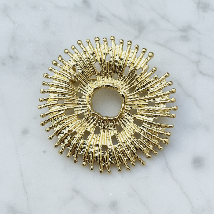 Gold sunburst decorative pin on a marble surface