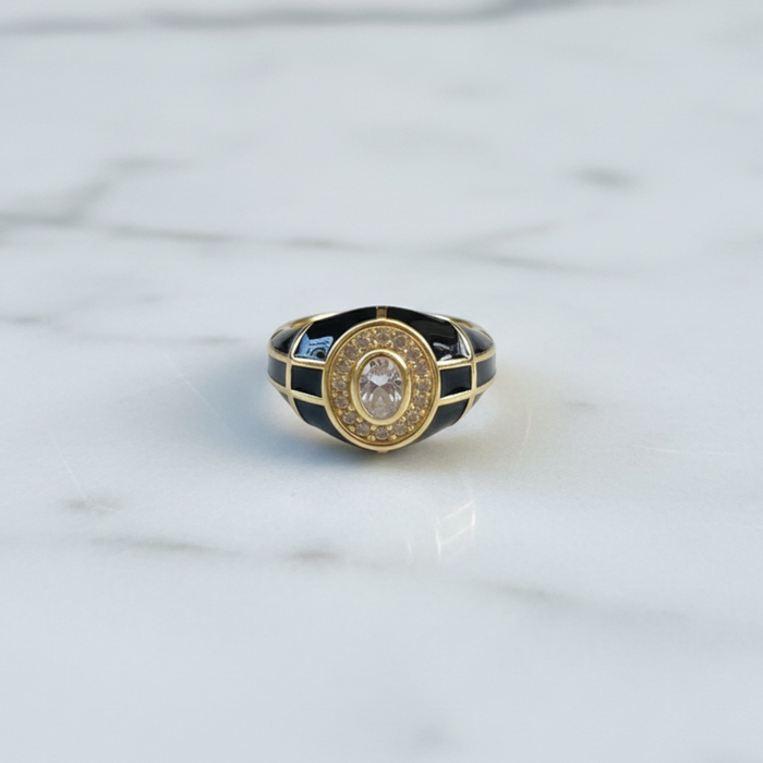 Gold ring with black and blue accents on a marble surface