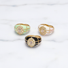 Three rings with different colored enameled settings on a light background