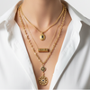 Woman wearing a white shirt with gold necklaces on a plain background