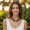 Woman wearing a white top and green necklace with a blurred natural background