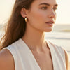 Woman wearing gold earrings with a blurred beach background