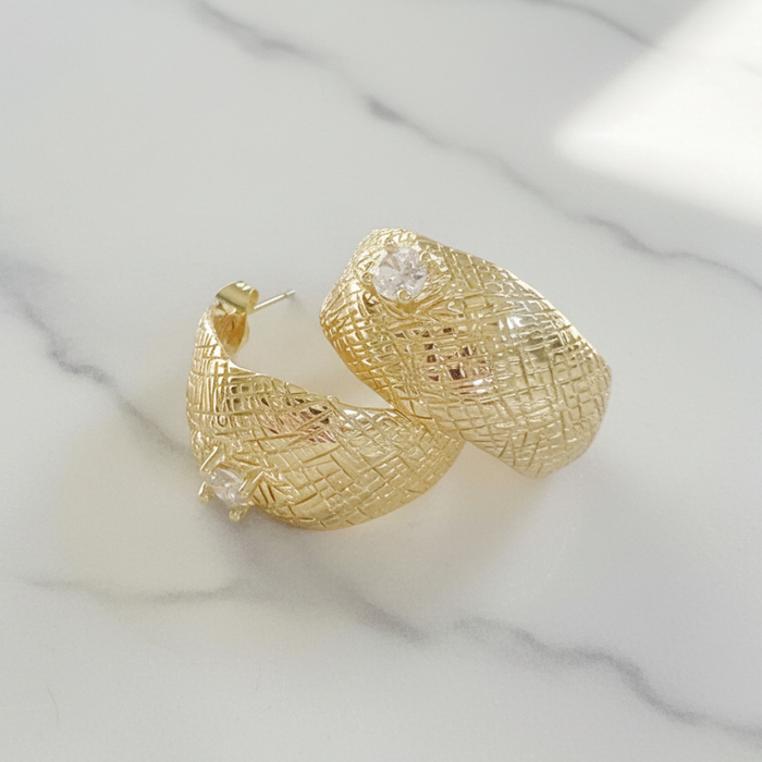 Gold hoop earrings with intricate design on a marble surface