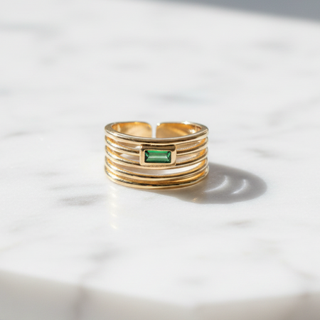 Gold ring with a green gemstone on a marble surface