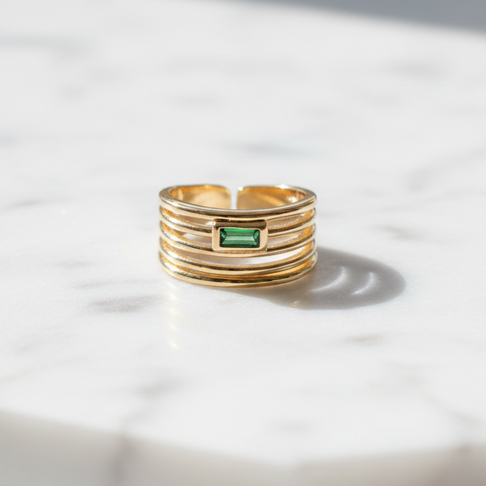 Gold ring with a green gemstone on a marble surface
