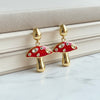 Mushroom-shaped earrings with red caps and gold stems on a marble surface.