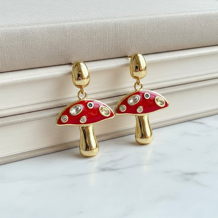Mushroom-shaped earrings with red caps and gold stems on a marble surface.