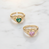 Two gold rings with heart-shaped gemstones on a light background