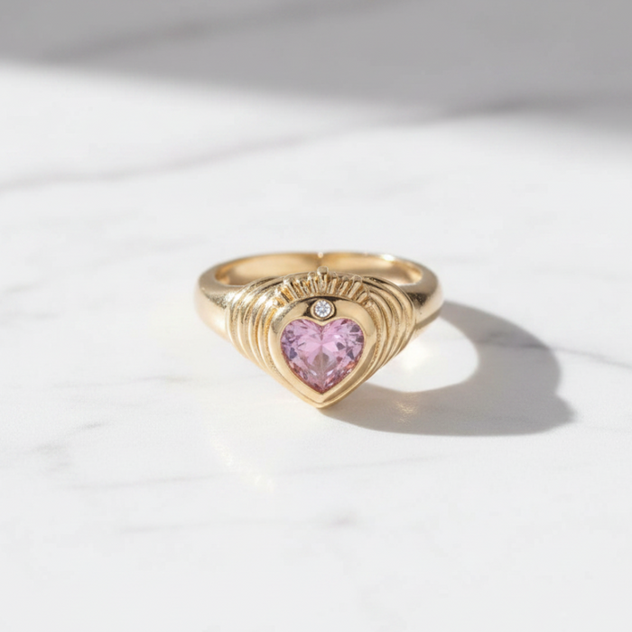 Gold ring with a heart-shaped pink gemstone on a light background
