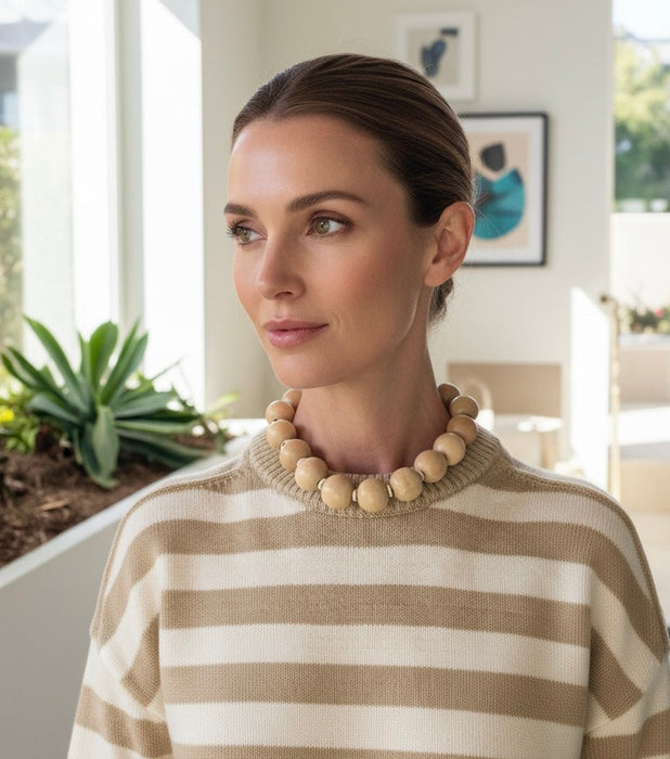 Woman wearing a striped sweater and wooden bead necklace indoors