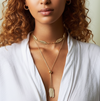 Woman wearing a gold necklace with a white top against a neutral background