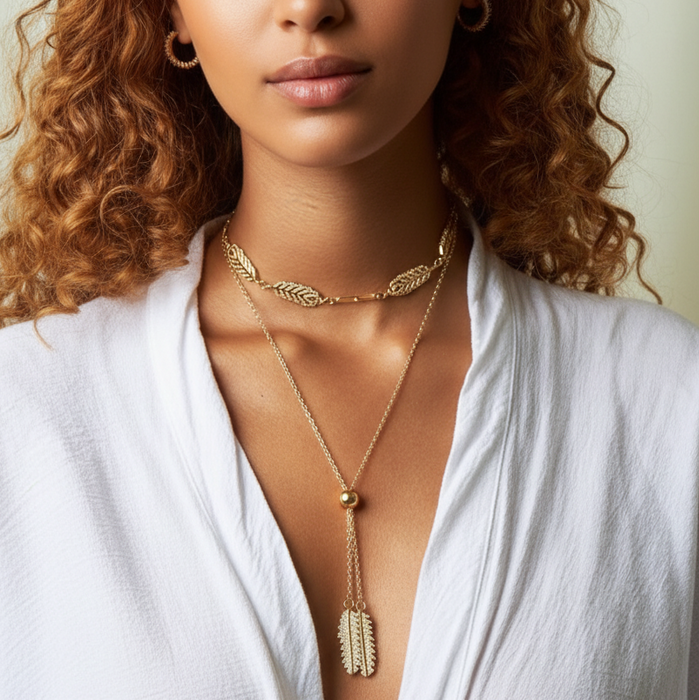 Woman wearing a gold necklace with a white top against a neutral background