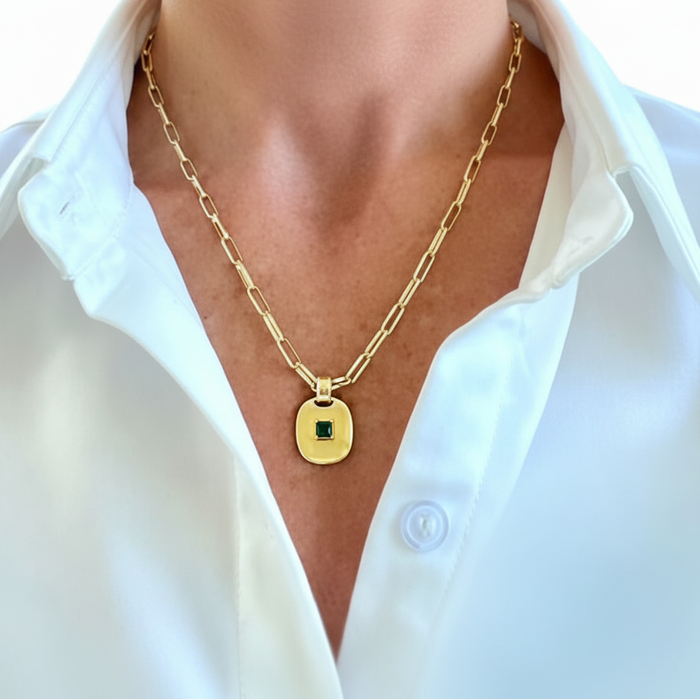 Gold chain necklace with a green gemstone pendant worn by a person in a white shirt.