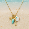 Gold necklace with charms on a sandy beach with shells and coral