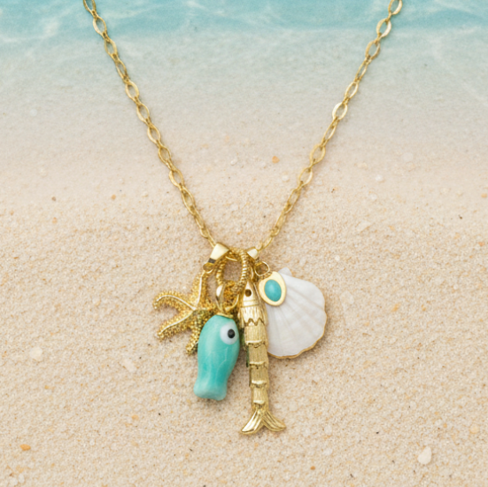 Gold necklace with charms on a sandy beach with shells and coral