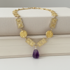Gold necklace with a purple pendant on a textured surface