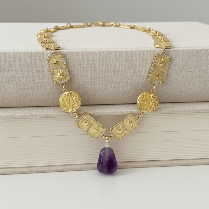 Gold necklace with a purple pendant on a textured surface