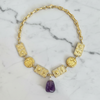 Gold necklace with a purple gemstone on a marble background