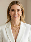 Woman wearing a white blazer and gold necklaces against a beige background