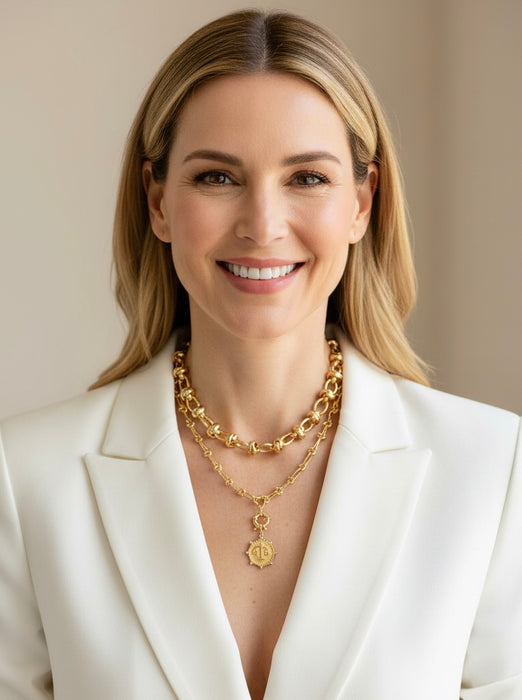 Woman wearing a white blazer and gold necklaces against a beige background