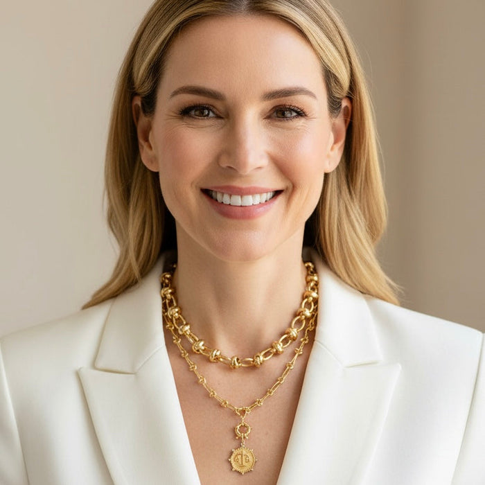 Woman wearing a white blazer and gold necklaces against a beige background