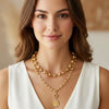 Woman wearing a gold necklace with a white top against a neutral background