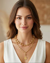 Woman wearing a gold necklace with a white top against a neutral background